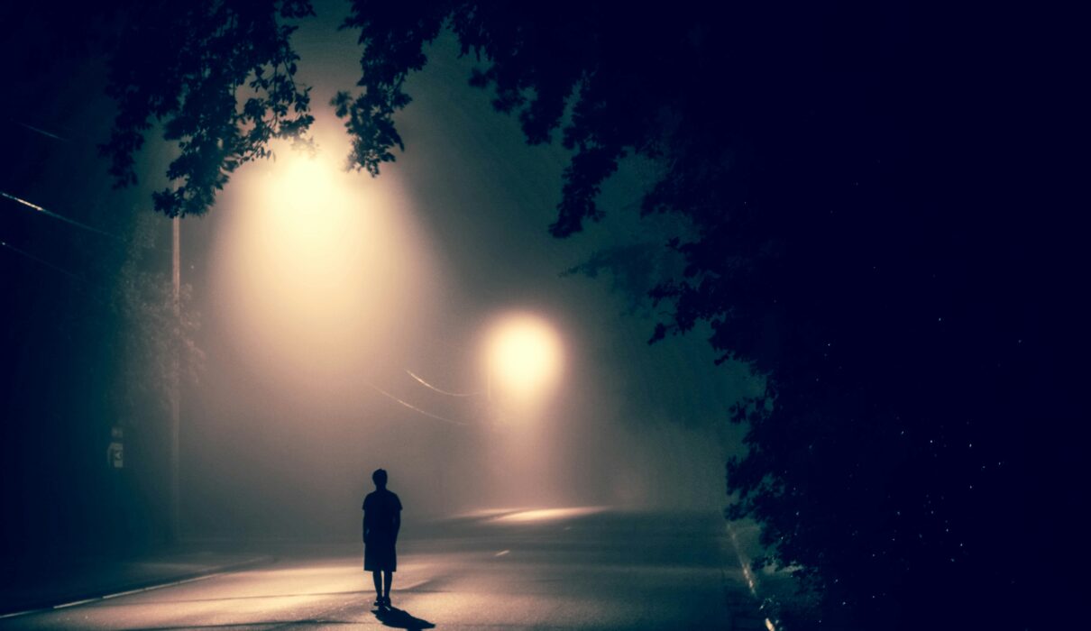 silhouette of person standing on concrete road with streetlights turned on during nighttime