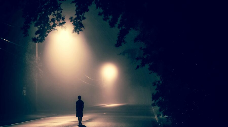 silhouette of person standing on concrete road with streetlights turned on during nighttime