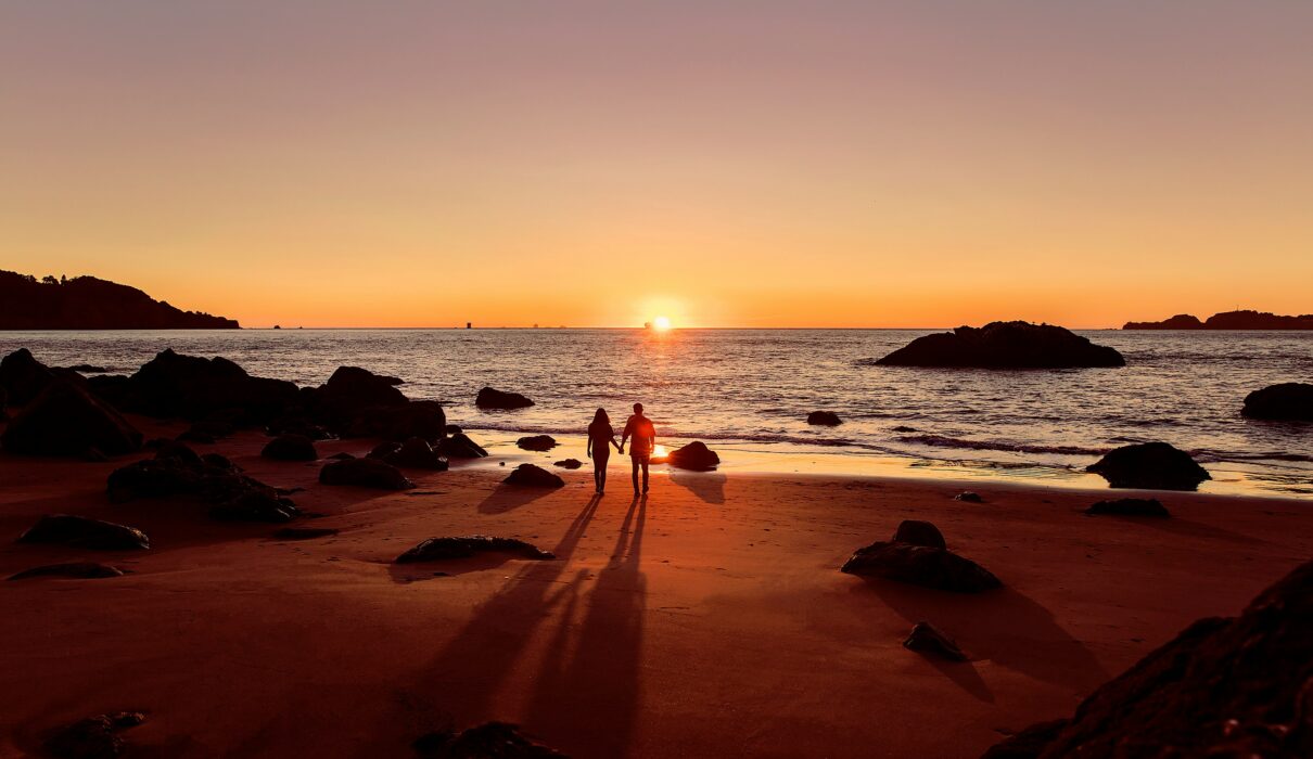 man in black shorts walking on beach during sunset