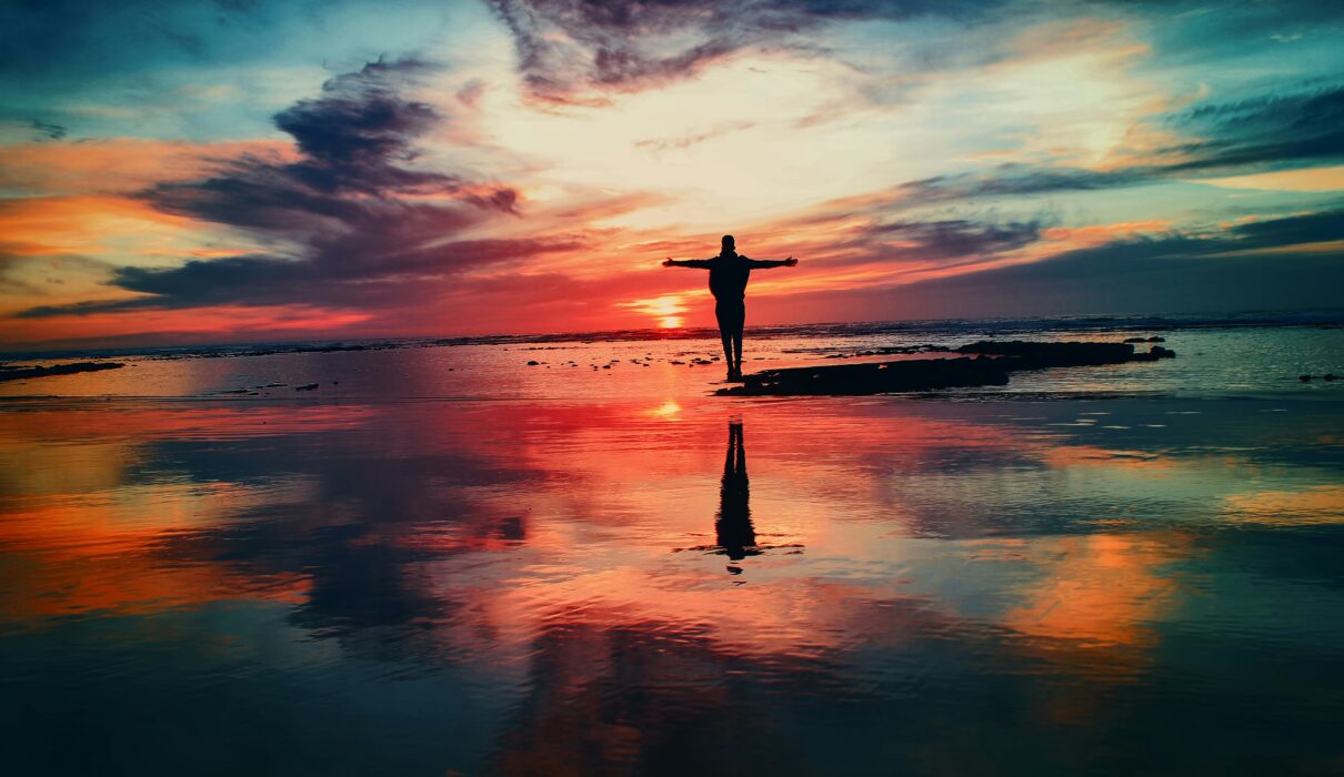 silhouette of person standing on rock surrounded by body of water