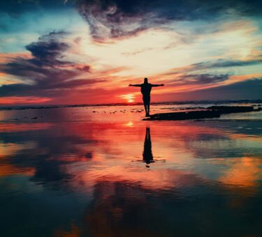 silhouette of person standing on rock surrounded by body of water