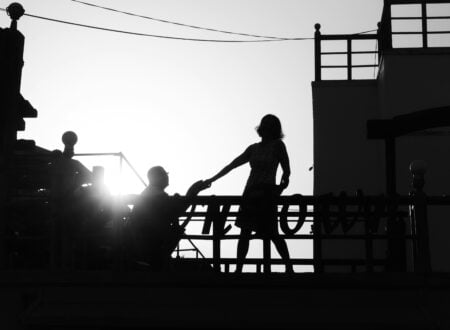 silhouette of girl standing near man kneeling beside railing