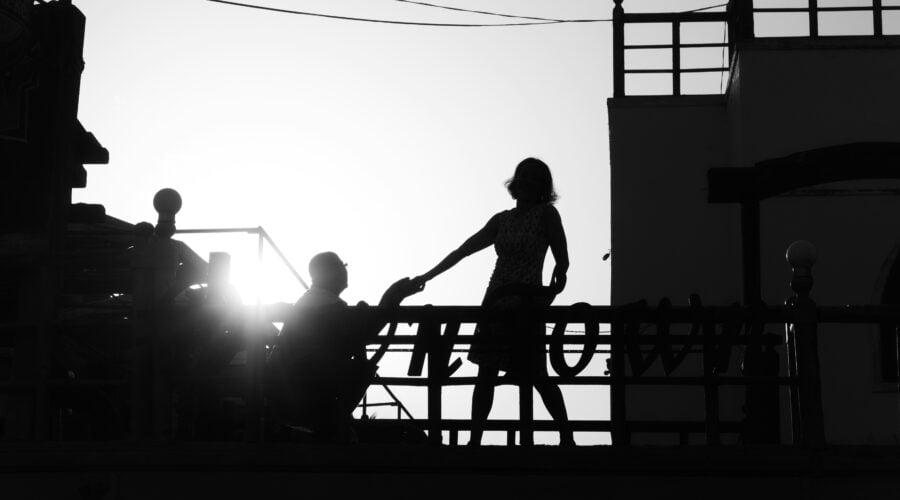 silhouette of girl standing near man kneeling beside railing