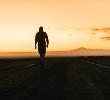 a man walking down a road at sunset