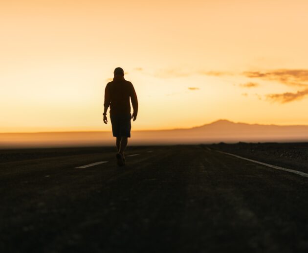 a man walking down a road at sunset